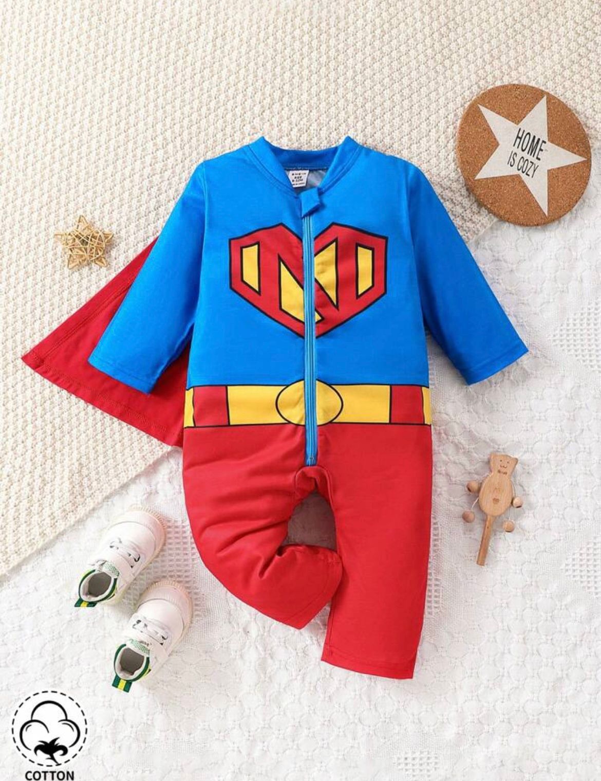 Superhero themed baby outfit with blue and red colors displayed on white knit background.