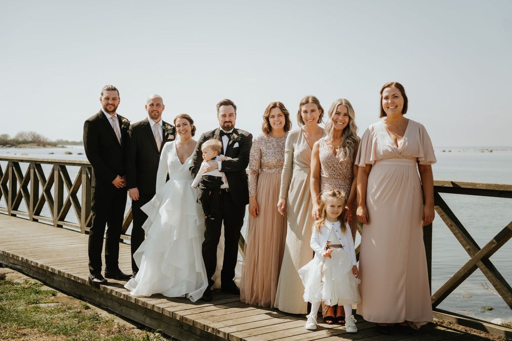 Wedding party poses together on wooden boardwalk by waterfront.