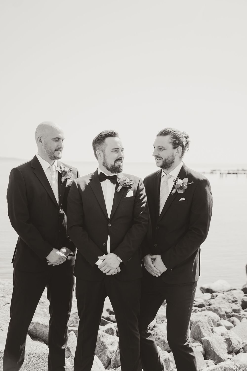 Black and white portrait of groomsmen laughing together by the ocean.
