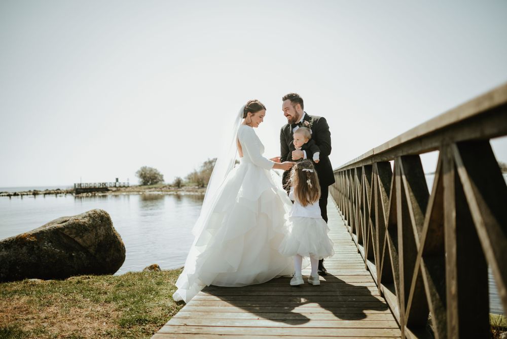 Bride and groom walk along wooden boardwalk by water during wedding.