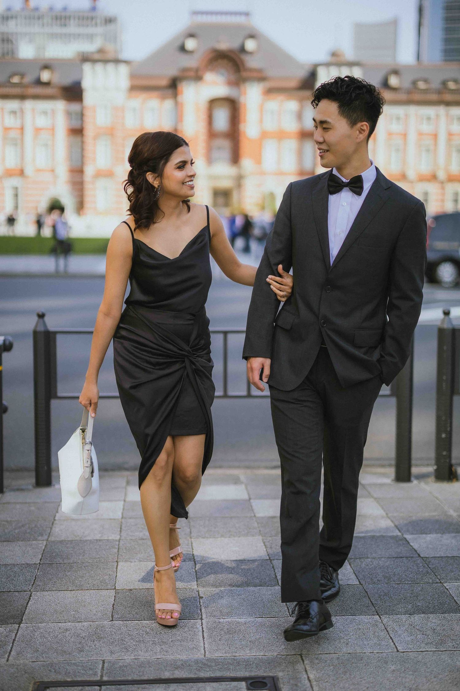 Elegantly dressed couple walking together near Tokyo Station at dusk.