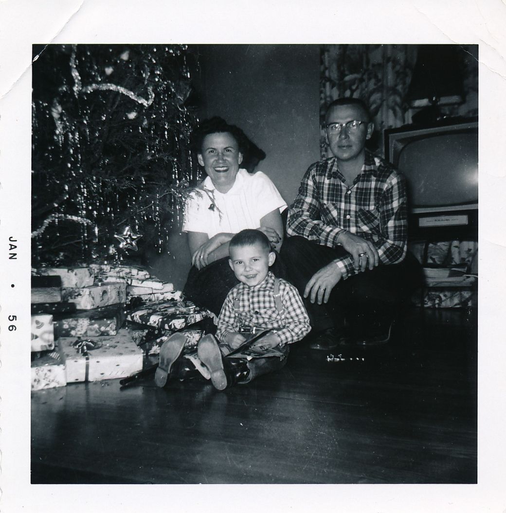 1950s black and white polaroid photo of family of 3 posing with smiles next to tinsel covered Christmas Tree