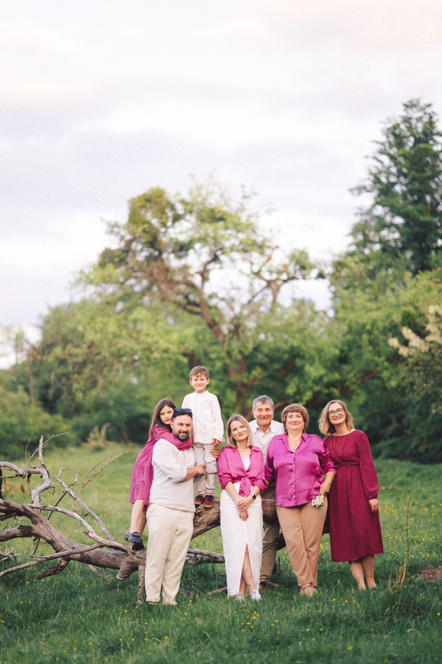 Family group portrait in coordinated pink and burgundy outfits posing outdoors.