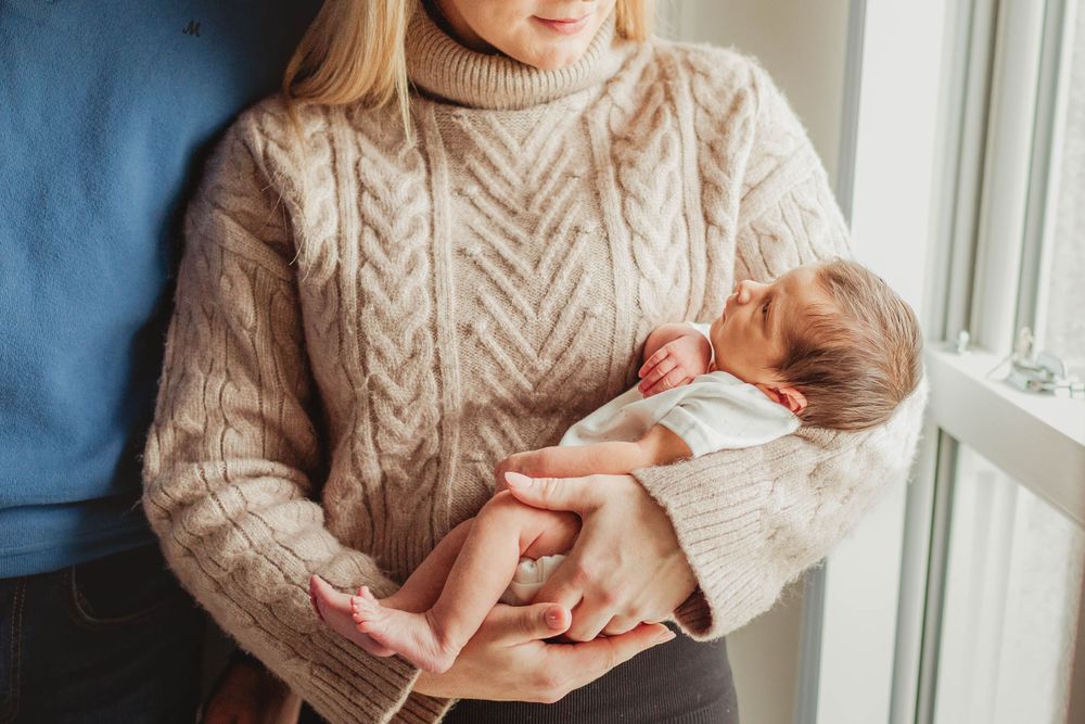 A cozy moment by the window with a baby being cradled in a knit sweater.