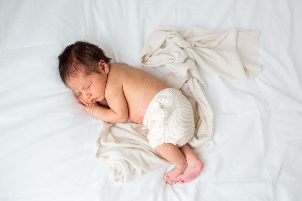 Newborn baby sleeping peacefully on white sheets in natural light.