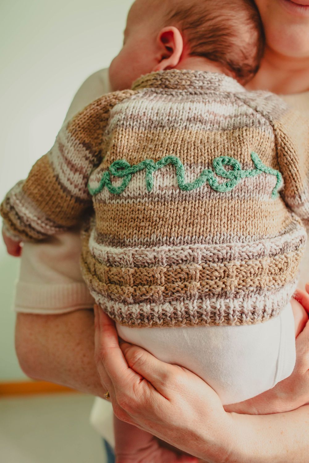 Close-up of a handmade knit baby sweater with mint green pattern detail.