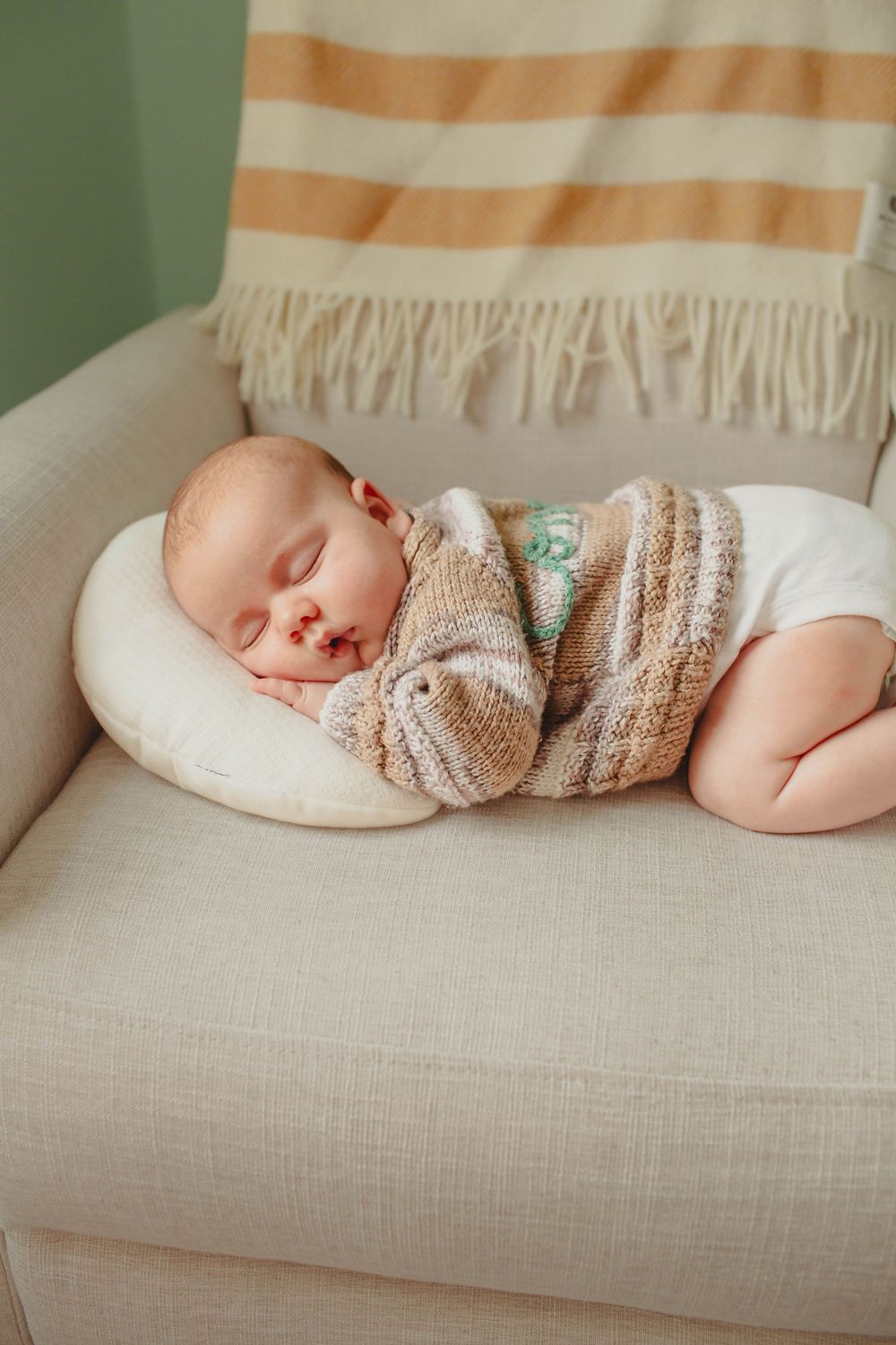 Sleeping baby wearing a knit sweater resting peacefully on a beige couch.