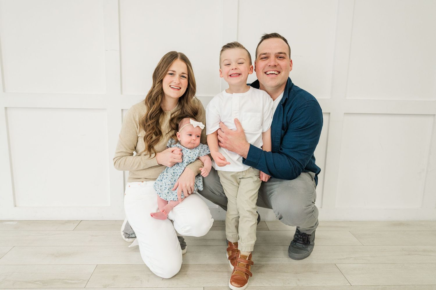 A loving family portrait with two young children in a bright indoor studio setting.