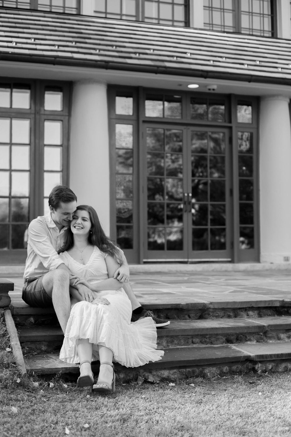 A couple in black and white shares tender moments while sitting on outdoor steps.