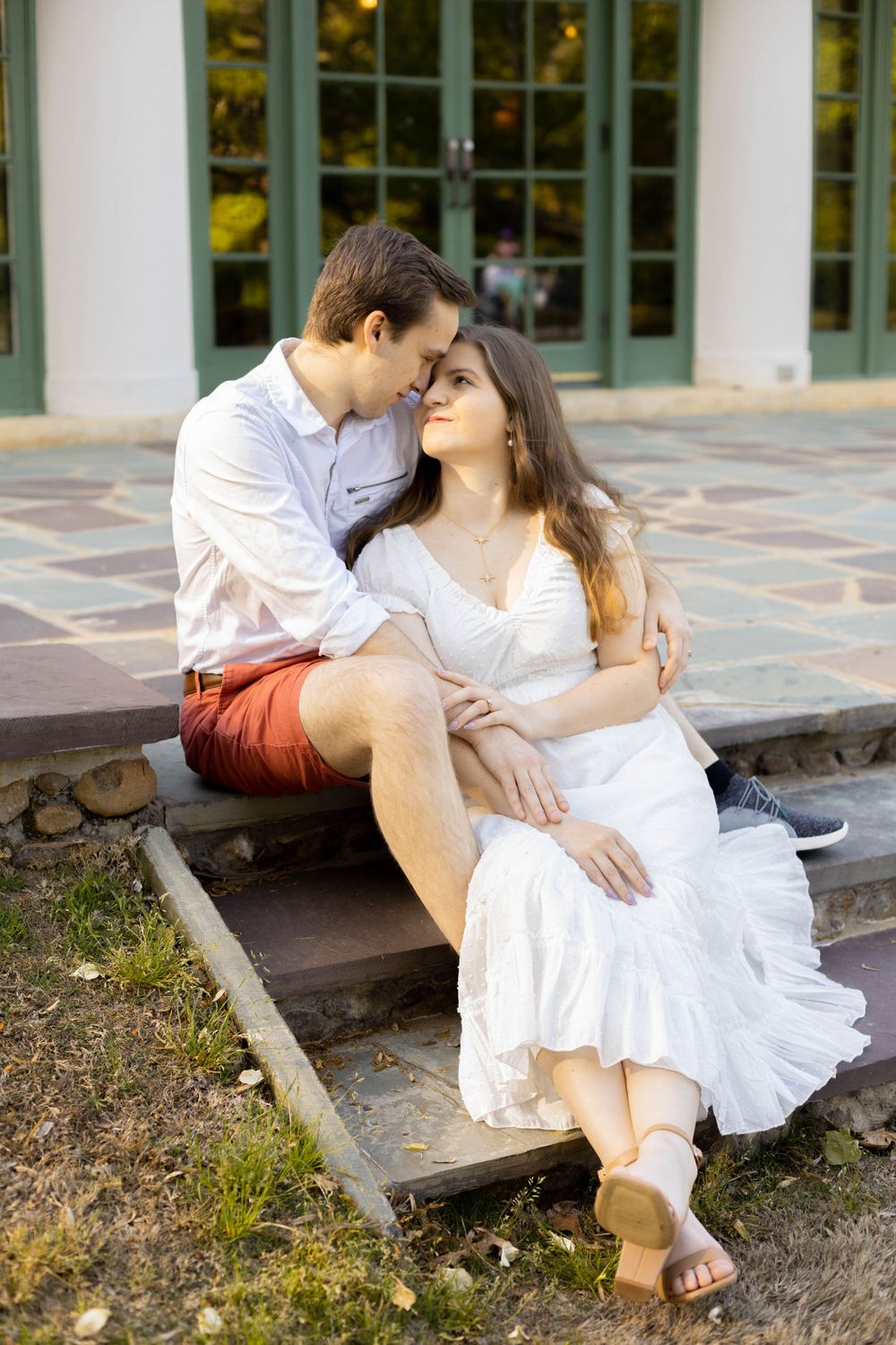 A couple in white clothing shares intimate moments on outdoor steps.
