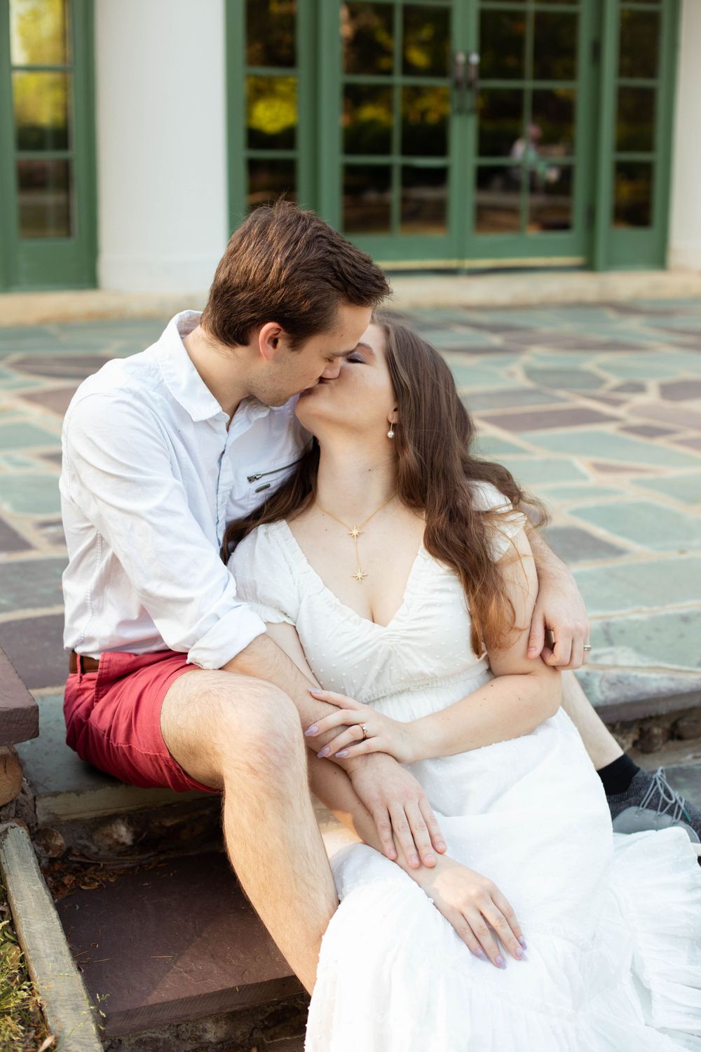 A romantic couple in white and red clothing embraces on stone steps.