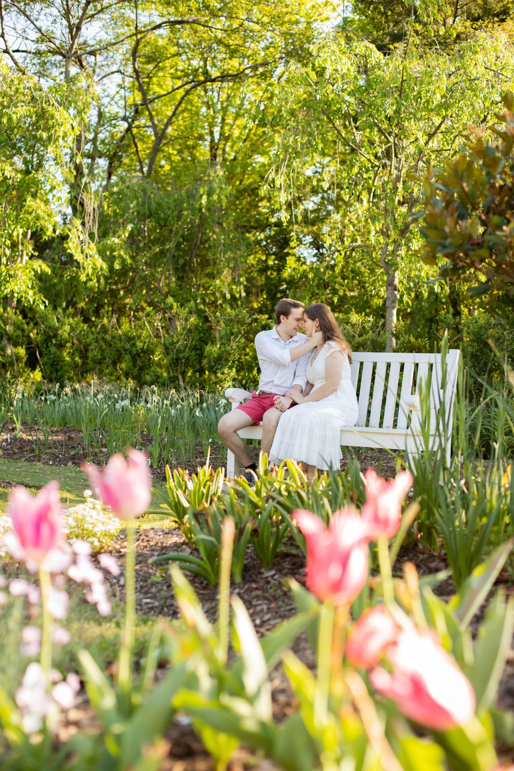 A couple shares romantic moments on a garden bench surrounded by blooming tulips.