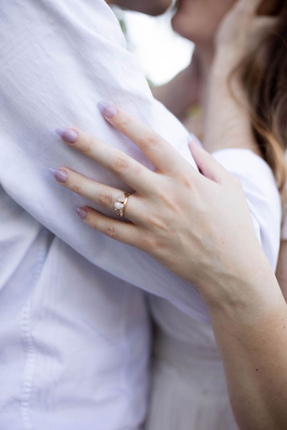 Close-up of hands wearing an engagement ring against a white shirt background.