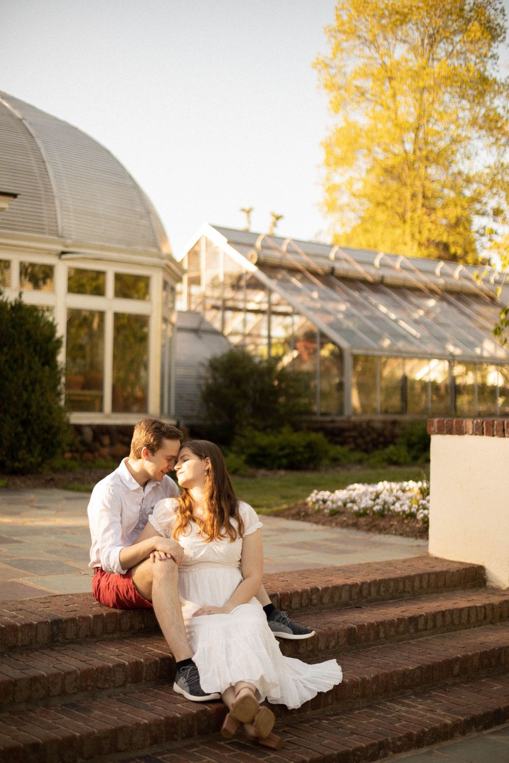 Couple sitting on brick steps during golden hour with autumn foliage in background.