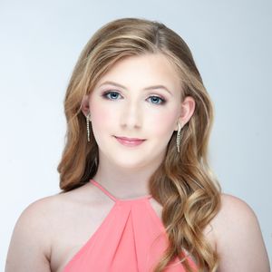 Portrait in soft lighting wearing a coral halter top with wavy styled hair and delicate earrings.