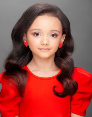 Studio portrait in red top with heart earrings and classic wavy hairstyle.