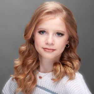 A studio portrait with soft lighting shows a person with wavy strawberry blonde hair wearing a white knit sweater. RED HAIR GIRL BLUE EYES