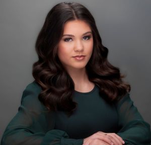 Professional portrait with dark brown wavy hair and emerald green blouse against neutral studio background. Won photogenic