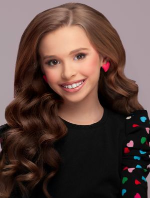 Glamour portrait of a teenager with wavy brown hair wearing a black top with colorful heart pattern details.