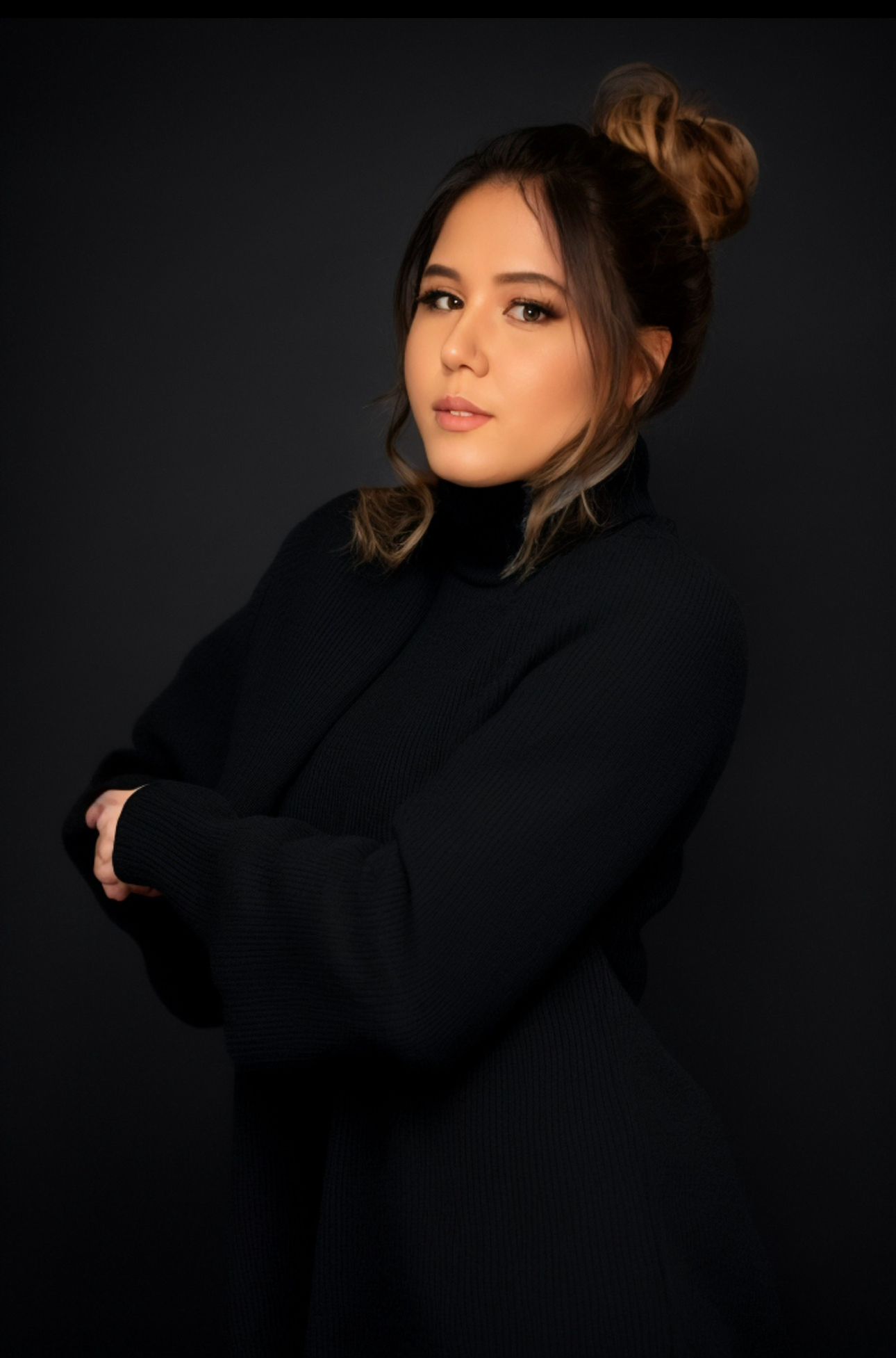 Professional studio portrait of a fashion model in black turtleneck sweater against dark background.
