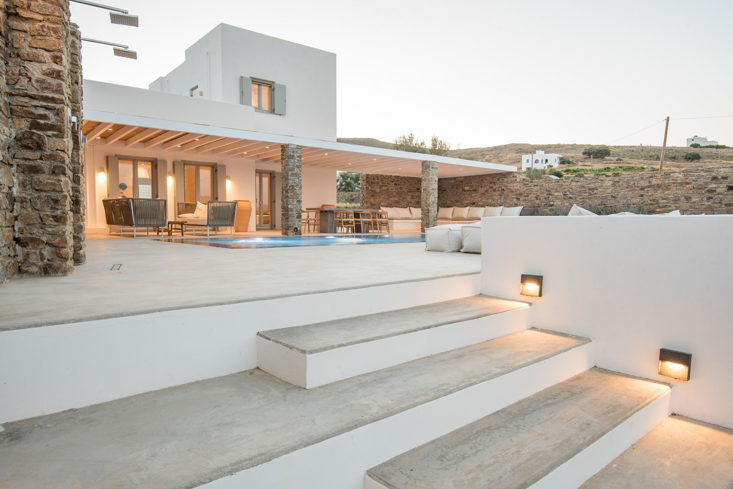 Modern Mediterranean villa exterior with illuminated white stone steps and covered patio area at sunset.
