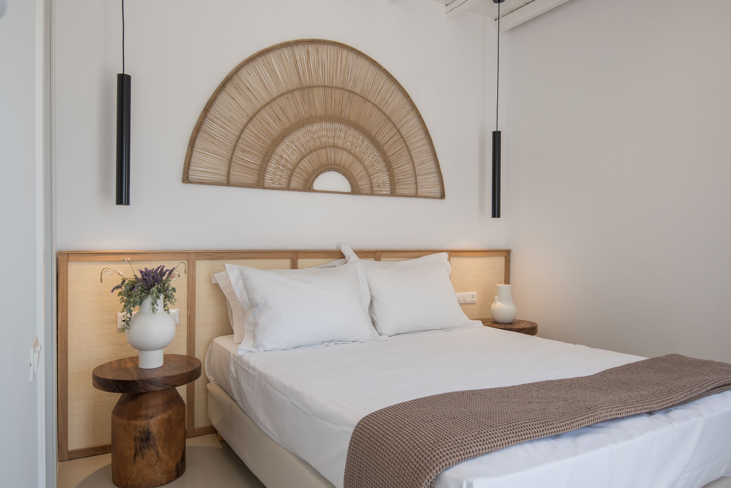 A serene bedroom with white bedding, wooden headboard, and decorative half-circle woven wall art above the bed.