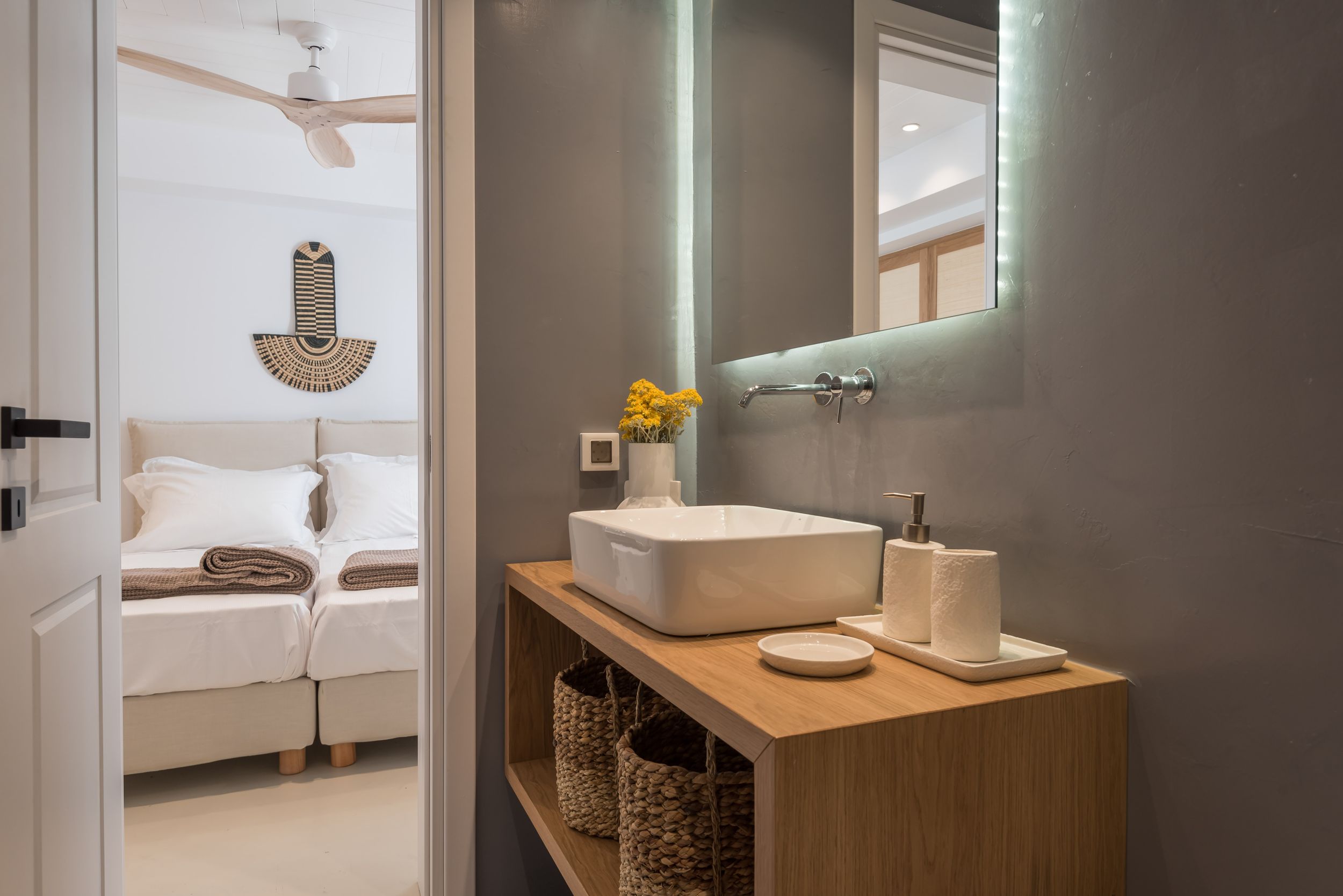 Modern bathroom interior with vessel sink on wooden vanity, illuminated mirror, and storage baskets in contemporary style.