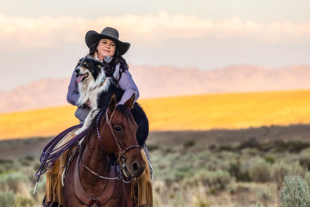 Rider and her dog on horseback against golden sunset in desert landscape.