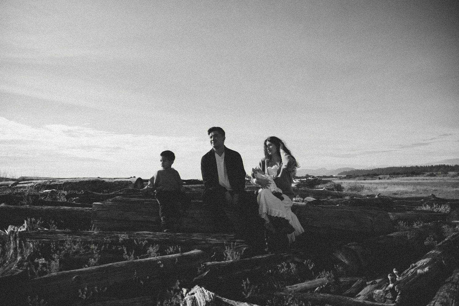 black and white panoramic photo of a family sitting on a log and looking out to the ocean during a family photoshoot in Vancouver, BC.