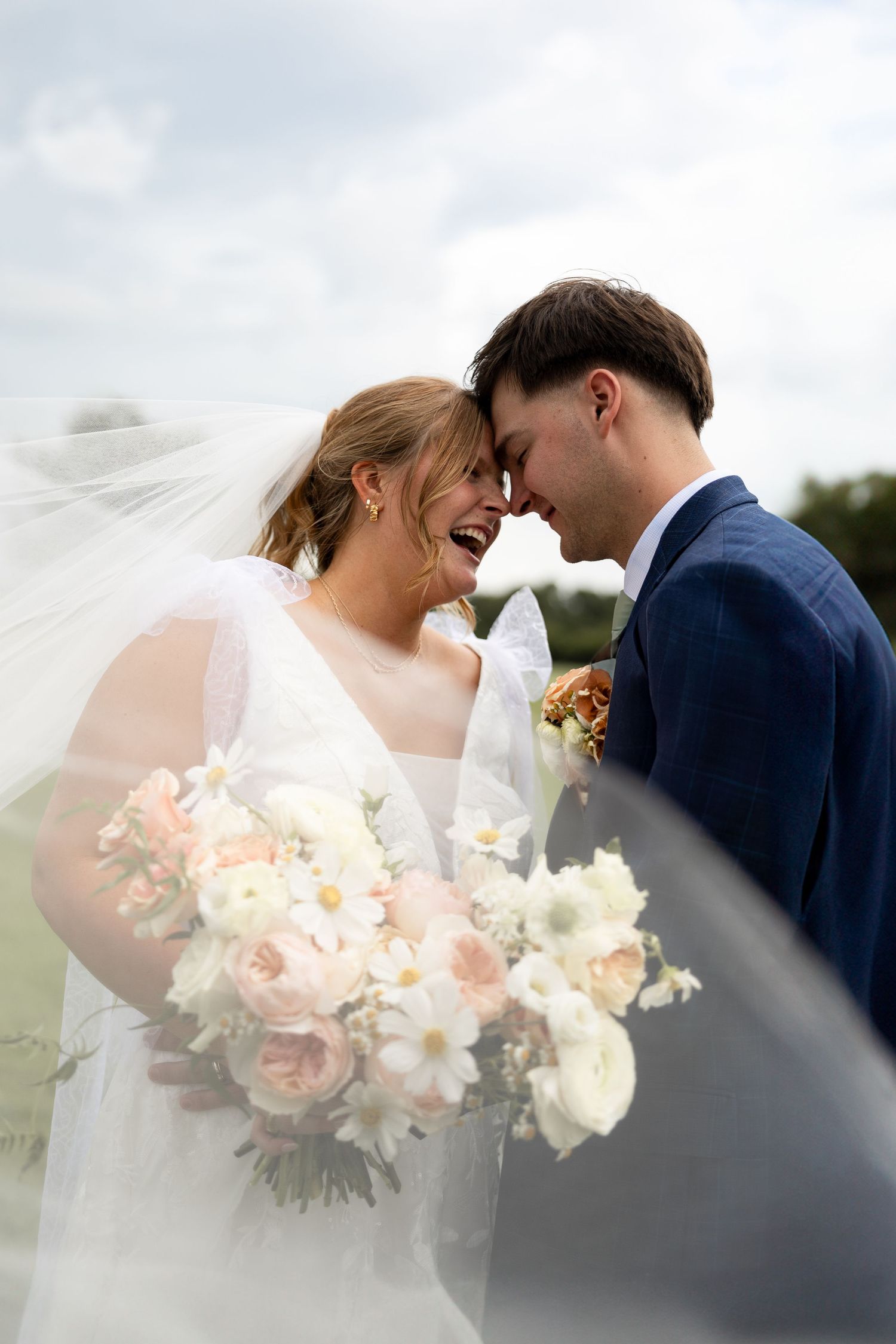 Tender moment between newlyweds outdoors with soft focus bouquet.