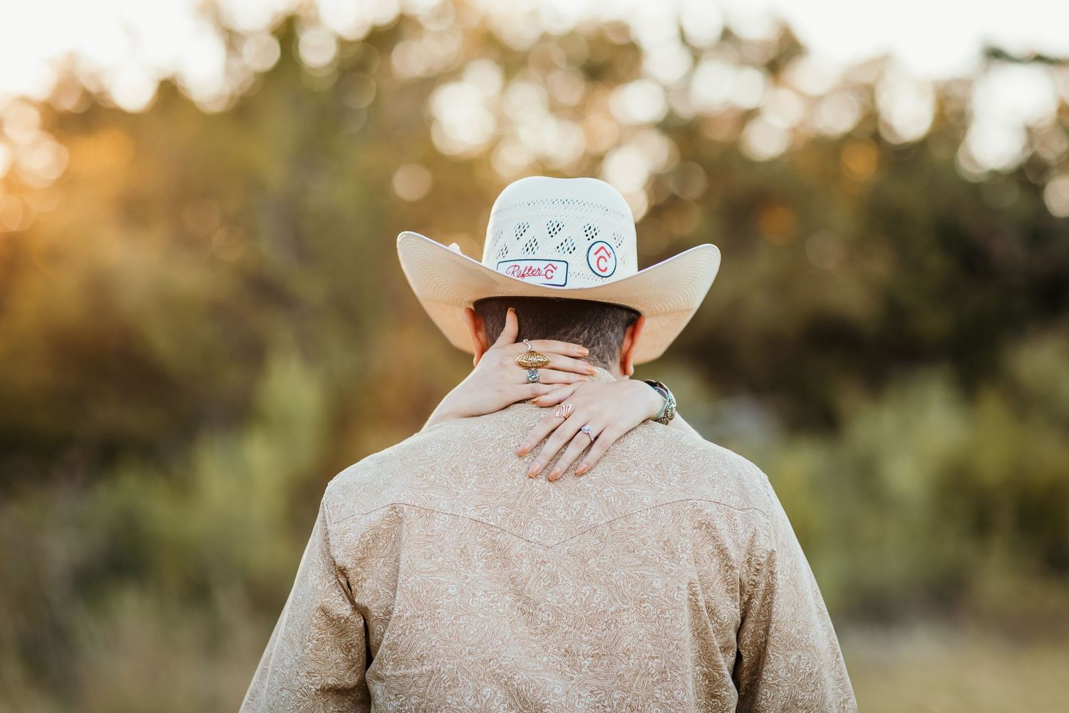 Person wearing a cowboy hat and tan jacket photographed from behind during golden hour sunset.
