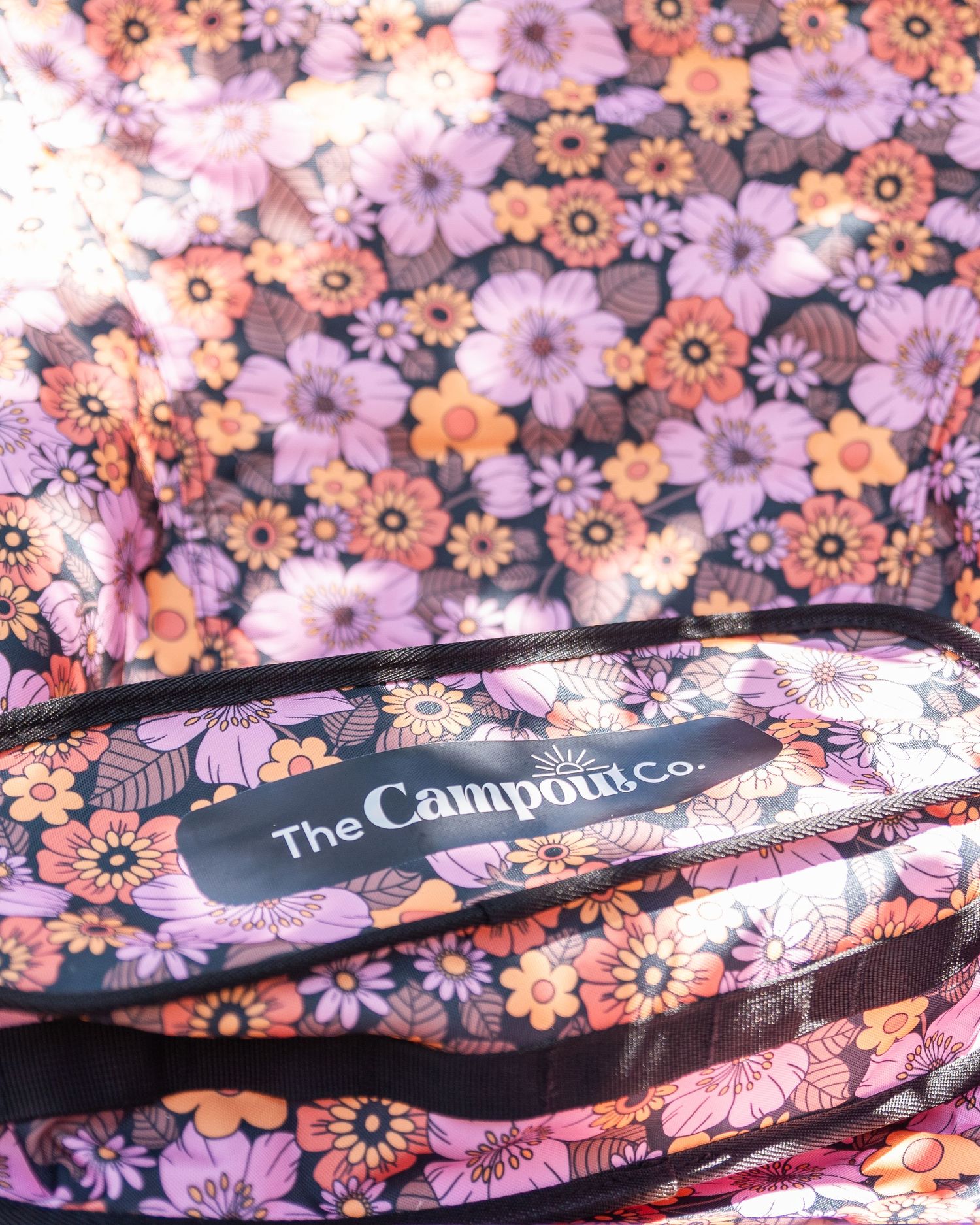 Close-up of floral patterned fabric with purple and orange flowers and The Campout Co logo.