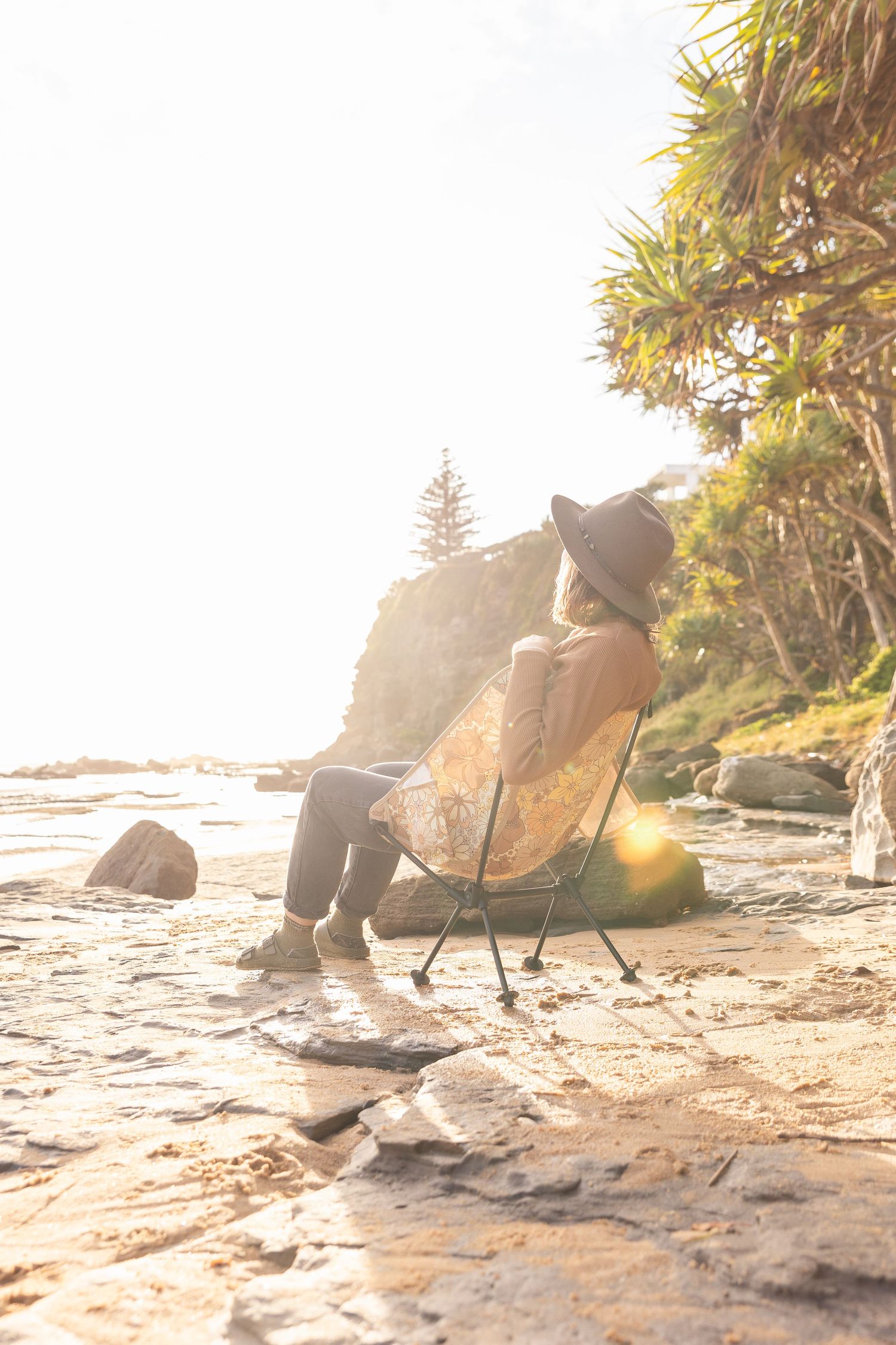 Sunlit beach scene with camping chairs positioned among coastal rocks.