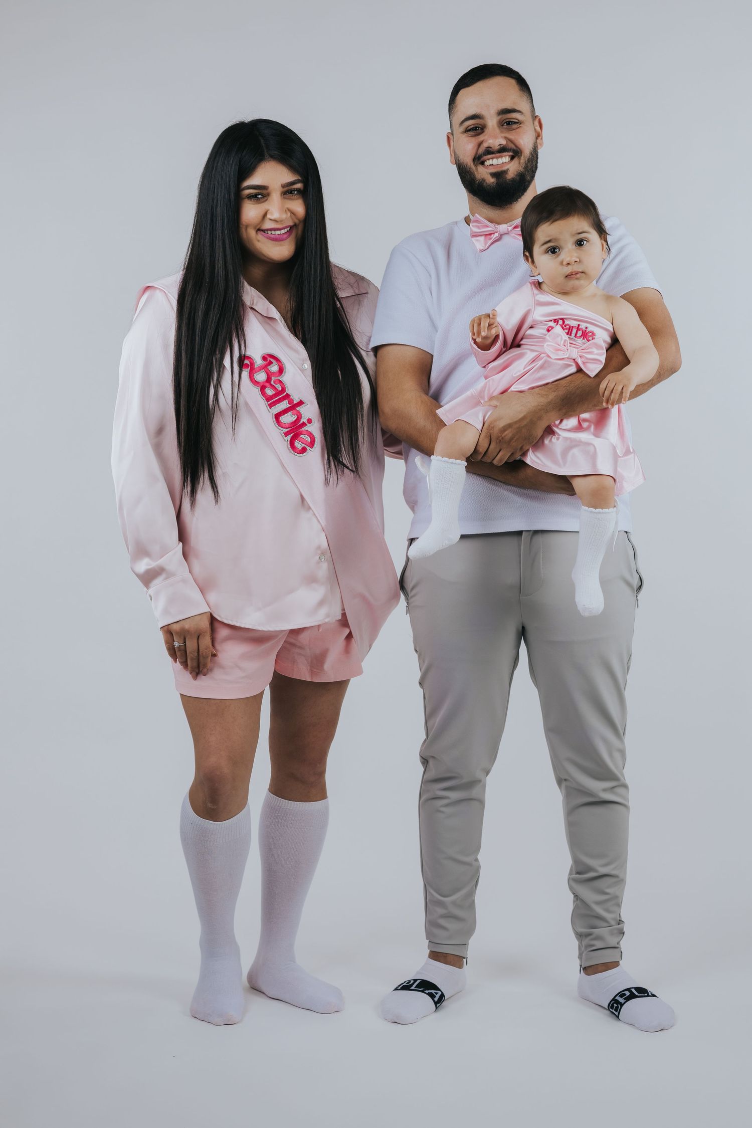 Family wearing matching pink and white outfits posing against grey backdrop.