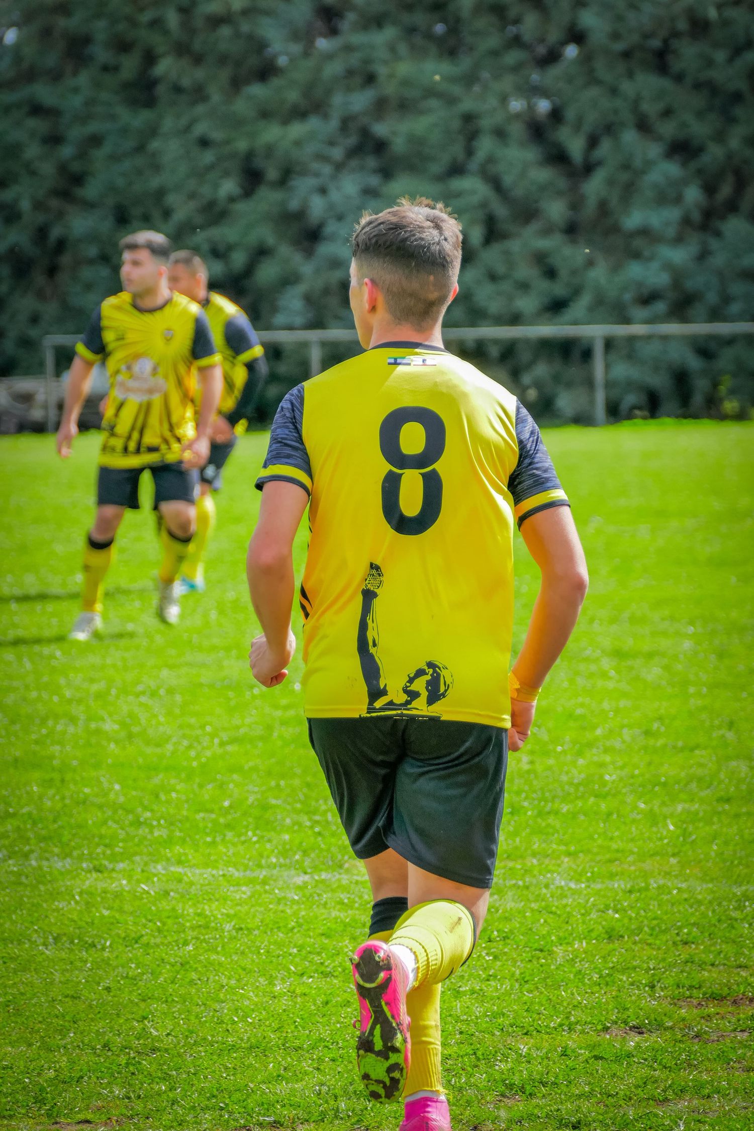 Youth soccer player wearing yellow number 8 jersey runs on green grass field during a match.