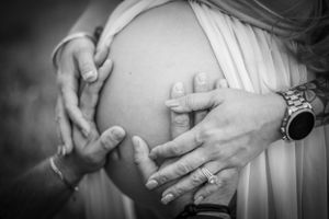 Black and white close-up of hands forming heart shape on pregnant belly. Geneva, Florida