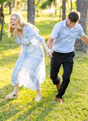A couple shares a playful moment running through a sunlit park, the woman wearing a flowing blue and white patterned dress. Geneva, Florida