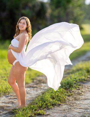 Maternity photo with flowing white dress billowing in the wind against natural backdrop. Geneva, Florida