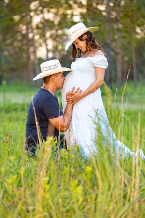A couple in western hats shares an intimate maternity moment in tall grass at sunset. Oviedo, Florida