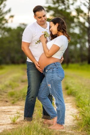 An expecting couple shares a tender moment on a dirt path surrounded by nature. Geneva, Florida