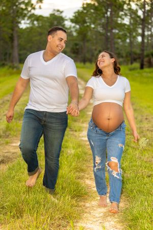 Expecting couple walking barefoot on a dirt path through green grass on a sunny day. Geneva, Florida