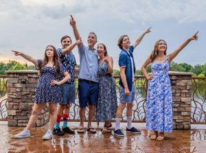 A family poses together on a wet deck wearing coordinated blue outfits while pointing upward.  Winter Springs, Florida