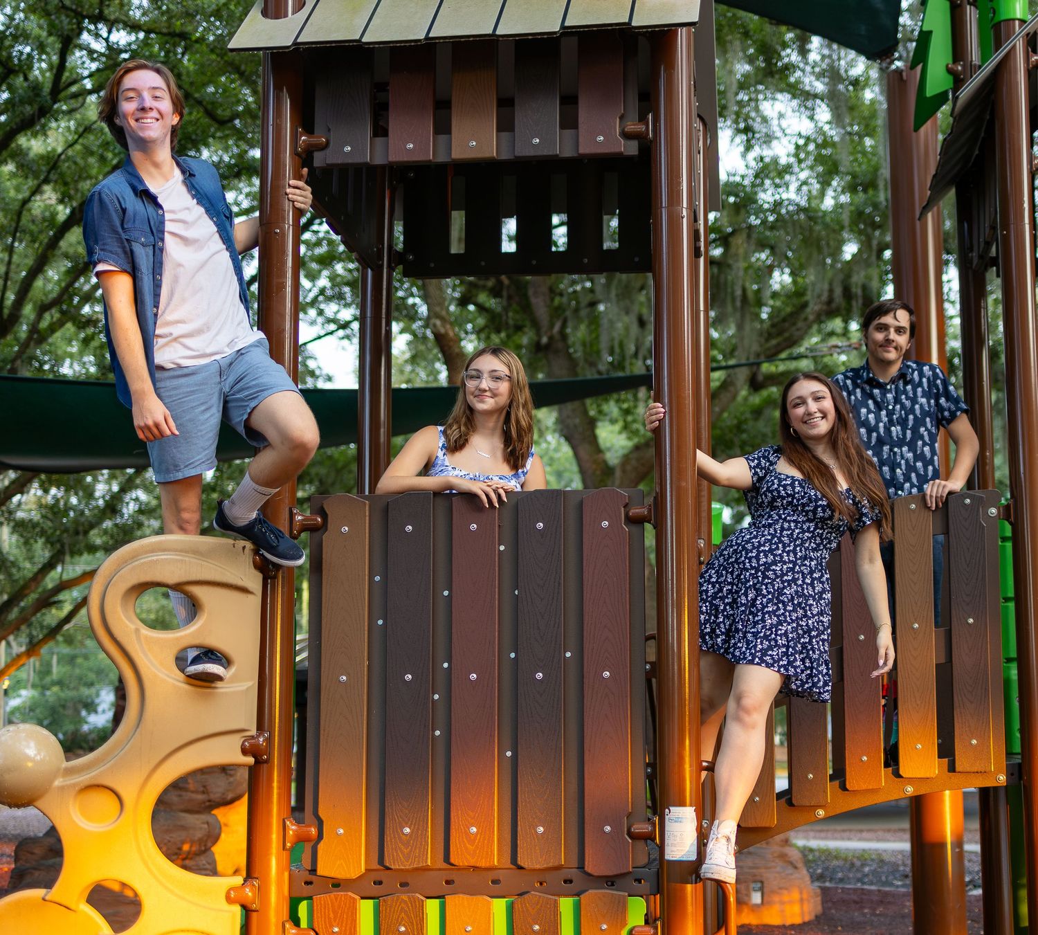 Family posing together on a wooden playground structure in casual summer attire. Winter Springs, Florida