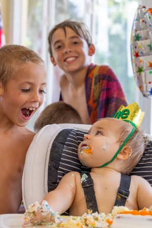 A joyful birthday celebration with children laughing around a baby covered in cake. West Palm Beach, Florida