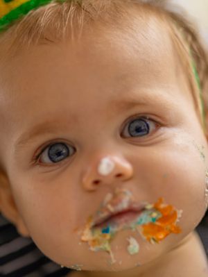 Close up of a baby with bright blue eyes and cake frosting on their face. West Palm Beach, Florida