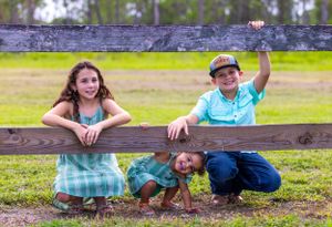 Three people posing playfully by a wooden fence in a park setting. Oviedo, Florida