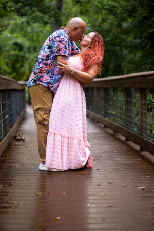 Romantic couple embrace on wooden bridge wearing coordinating pink and floral outfits. Geneva, Florida