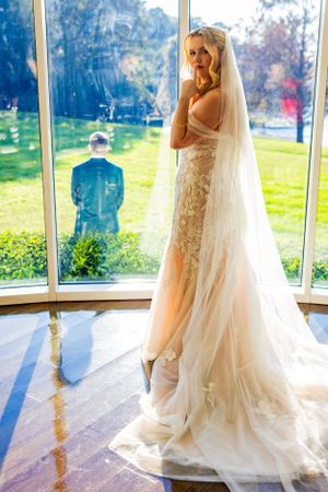 Elegant bride in lace gown and cathedral veil poses in sunlit window bay. Lake Mary, Florida