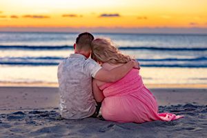 A couple sits together on the beach during a vibrant orange sunset. Cape Canaveral, Florida