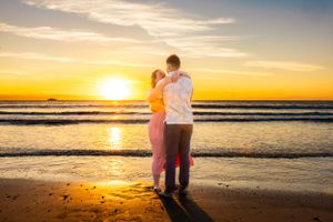 Silhouetted figures embrace on beach at sunset with waves in background. Cape Canaveral, Florida